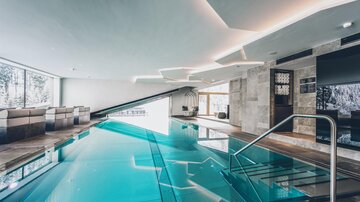 Ein eleganter Innenpool mit klarem Wasser und modernen Designelementen. Großen Fensterflächen sorgen für viel Tageslicht und einen Blick ins Freie. | © elizabeth.at