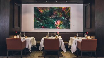 Ein elegantes Restaurant mit gedeckten Tischen und stilvollen Stühlen. An der Wand hängt ein großes, farbenfrohes Kunstwerk. | © elizabeth.at
