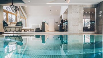 Ein eleganter Innenraum mit einem klaren Pool und bequemen Möbeln. Große Fenster sorgen für viel Tageslicht und eine entspannte Atmosphäre. | © elizabeth.at