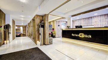 A modern hotel lobby with wooden details and a reception desk. The reception is bright and inviting, with decorative plants.