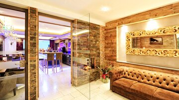 A modern living room with a comfortable couch and elegant wooden elements. The room is brightly lit and features large windows.