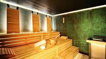 A modern sauna with bright wooden loungers and soft lighting. The walls are designed in a calming green shade.