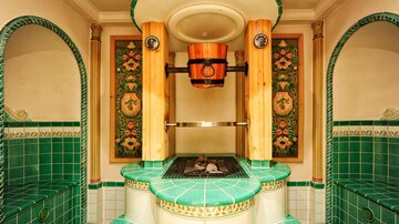 An elegant room with green tiles and decorative walls. In the center, there is a sauna with a wooden stove and a relaxing atmosphere.