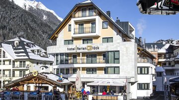 A modern hotel in the Alps, surrounded by snow-covered mountains. In front of the hotel, there is a terrace with guests enjoying the winter landscape.