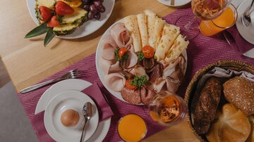 An attractively arranged breakfast table with sausage, cheese, and fresh fruit. In addition, there are various breads and beverages.