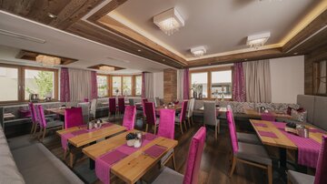 A modern restaurant with bright wooden elements and colorful, pink chairs. Large windows let in plenty of light and create a friendly atmosphere.
