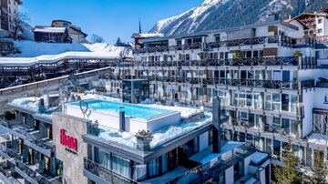Ein modernes Hotel mit einer Dachterrasse und einem Pool, umgeben von schneebedeckten Bergen. Die Einrichtungen wirken einladend und stilvoll.