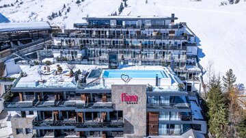 Ein modernes Hotel in den Bergen mit einem Außenpool und Balkonen. Der Schnee um das Gebäude herum sorgt für eine schöne winterliche Atmosphäre.