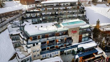 Ein modernes Hotel im Schnee mit einem Pool auf dem Dach. Die Umgebung ist winterlich und malerisch.