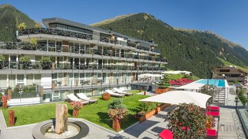 Ein modernes Hotelgebäude mit Balkonen und einem Pool in einer schönen Berglandschaft. Der Außenbereich ist mit Liegen und Pflanzen gestaltet.
