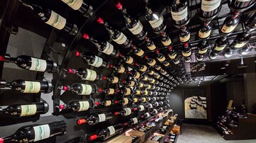 Ein Weinkeller mit vielen Flaschen Rotwein, die an einer runden Wand hängen. Die Atmosphäre ist elegant und einladend.