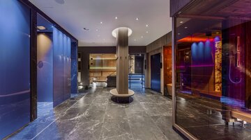 Ein eleganter Wellnessbereich mit modernen Saunen und einem stilvollen Empfangsbereich. Der Boden ist aus dunklem Marmor und die Wände leuchten in sanften Farben.