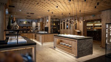 Ein modernes Restaurant mit Holzinterieur und eleganten Lichtanlagen. Die Einrichtung ist stilvoll und einladend, ideal für gemütliche Mahlzeiten.
