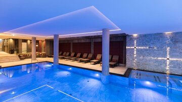 Ein moderner Wellnessbereich mit einem blauen Pool und gemütlichen Liegen. Die Beleuchtung erzeugt eine entspannende Atmosphäre.