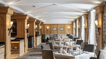 Ein elegantes Restaurant mit Holzelementen und gemütlicher Atmosphäre. Die Tische sind schön gedeckt und sorgen für ein einladendes Ambiente.