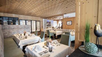 Ein elegantes Restaurant mit schön gedeckten Tischen und einem gemütlichen Ambiente. Die Holzelemente und die Sanftheit der Farben schaffen eine einladende Atmosphäre.