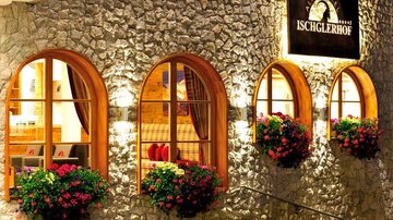 Ein einladendes Hotel mit Natursteinfassade und großen Fenstern. Bunte Blumenkästen schmücken den Eingang und verleihen eine gemütliche Atmosphäre.