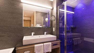 Ein modernes Badezimmer mit einem großen Waschbecken und stilvollen Armaturen. Die Dusche ist durch Glaswände abgetrennt und wird von blauem Licht beleuchtet.