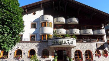 Ein charmantes Hotel mit einem einladenden Eingang und Balkonen. Bunte Blumen schmücken den Außenbereich und der Himmel ist klar und blau.