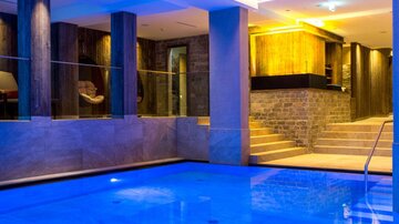 Ein elegantes Schwimmbad mit blauem Wasser und modernen Designelementen. Der Raum ist stilvoll beleuchtet und bietet eine entspannende Atmosphäre.