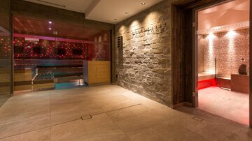 Ein eleganter Wellnessbereich mit einem Pool und stimmungsvollem Licht. Der Raum hat eine moderne, beruhigende Atmosphäre mit Steinwänden und Holzdetails.
