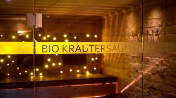 Ein entspannender Raum mit warmem Licht, der als Bio Kräutersauna dient. Die Wände sind aus Stein, und ein ätherisches Ambiente lädt zur Erholung ein.