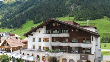 Ein schönes Hotel mit traditioneller Architektur inmitten von grünen Bergen. Rundherum befinden sich gemütliche Terrassen und blühende Blumen.