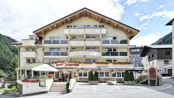 A cozy hotel with an inviting entrance. The facade is bright and designed in typical alpine style, surrounded by mountains.