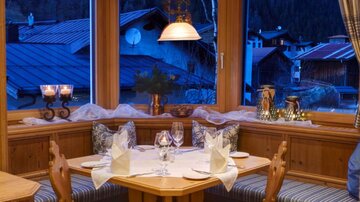 A cozy dining area with wood paneling and windows that offer a view of a tranquil landscape. The table is set for dinner, and the atmosphere is warm and inviting.