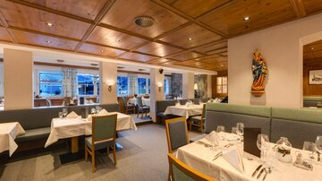 A cozy restaurant with wooden paneling and set tables. Bright windows create an inviting atmosphere.