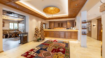 An inviting hotel lobby with a wooden reception desk and a colorful carpet. On the walls, warm lighting and stylish decorations can be seen.