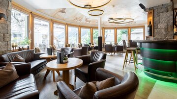 A stylish interior with comfortable leather chairs and round wooden tables. Large windows provide plenty of natural light and a pleasant atmosphere.