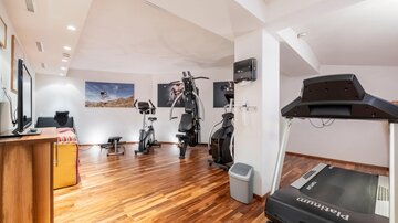A modern gym with various exercise equipment. The room has a wooden floor and a bright, inviting atmosphere.