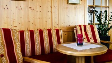 A cozy seating area with red and gold upholstered armchairs. A round wooden table is in the center, decorated with a glass.