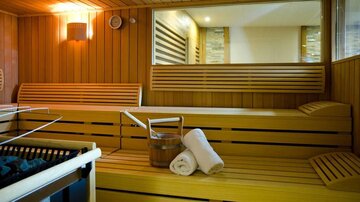 A cozy sauna with wooden paneling. In the room, towels and a wooden container can be seen.