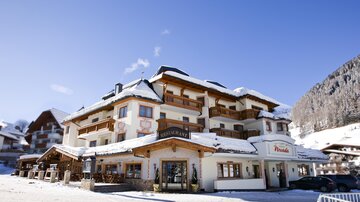 A cozy hotel in a snowy landscape. The facade is designed in a traditional style with balconies and wooden details.