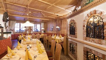 A cozy restaurant with wooden decor and warm lighting. The tables are set with yellow tablecloths and napkins.