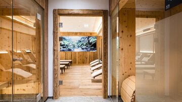 A relaxing wellness area with wooden details and comfortable loungers. In the background, a calming landscape is displayed on a screen.