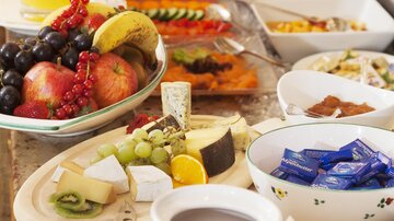 A rich breakfast buffet with fresh fruit, yogurt, and various delicacies. In the background, juices and sweet dishes are prepared.