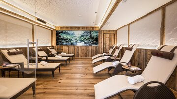 A relaxing wellness room with loungers and a calming view of a natural landscape. Wooden elements create a cozy atmosphere.