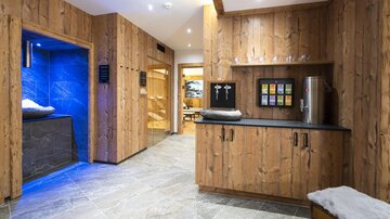 A stylish wellness area with wooden paneling and soft lighting. On the left side, there is an elegant room with blue light accents.