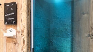 A modern steam sauna area with a dark stone floor and a bench. Soft towels are ready, while gentle light illuminates the room.