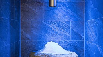 A stylish spa with blue lights and an oversized rock covered in a layer of snow. The walls are clad in dark stone tiles.
