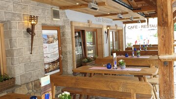 An inviting café-restaurant with rustic wooden tables and a cozy atmosphere. The tables are decorated with blue vases and checked tablecloths.