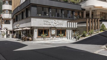 A modern hotel building called "Hotel Sonne". It is located at a street corner and has an inviting outdoor area with tables.