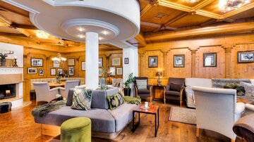 An elegant living room with wooden walls and cozy seating. There is a fireplace and decorative pictures on the wall.