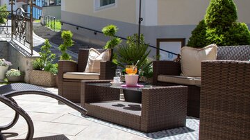 A cozy outdoor area with rattan furniture and an umbrella. Green plants create an inviting atmosphere.