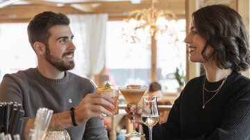 A cozy bar evening with two people sitting at the bar and clinking their drinks. A warm atmosphere with stylish interior.