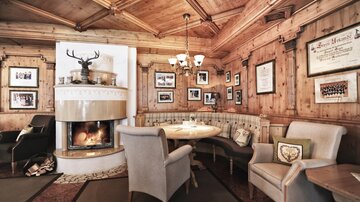 A cozy room with a wooden ceiling and an inviting seating area. A fireplace creates a warm atmosphere, and various pictures hang on the walls.