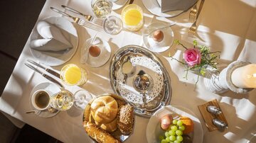 A beautiful breakfast table with various foods, including rolls, grapes, and eggs. There are also drinks like coffee and fruit juices.